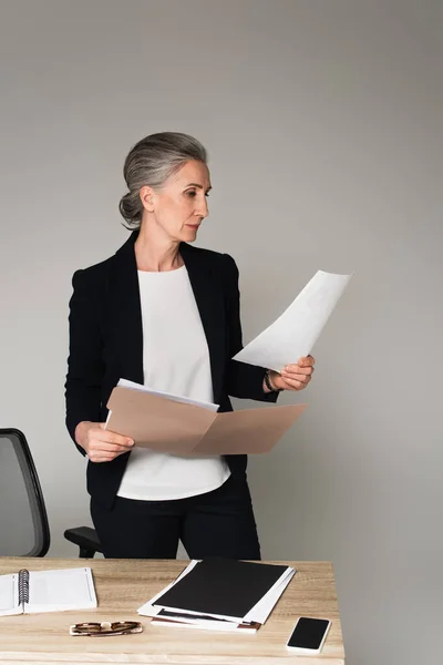 Manager hält Papiermappe in der Nähe von Smartphone und Notizbuch auf Tisch isoliert auf grau — Stockfoto