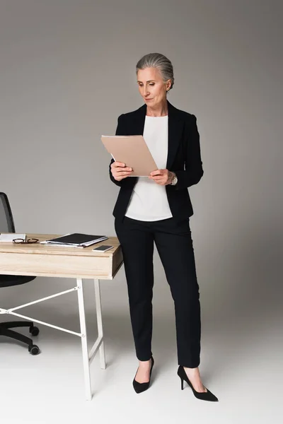 Geschäftsfrau betrachtet Dokumente am Tisch auf grauem Hintergrund — Stockfoto
