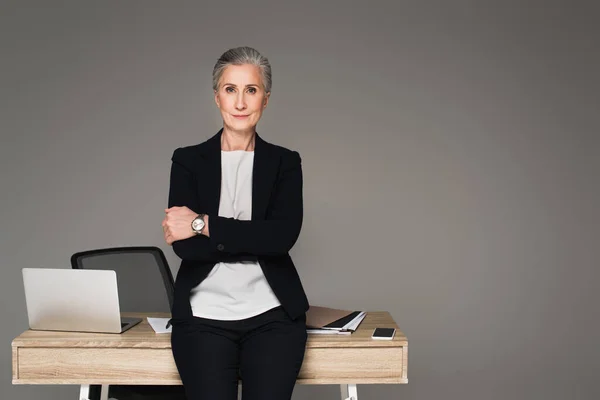 Femme d'affaires debout près des gadgets et des documents sur la table isolé sur gris — Photo de stock