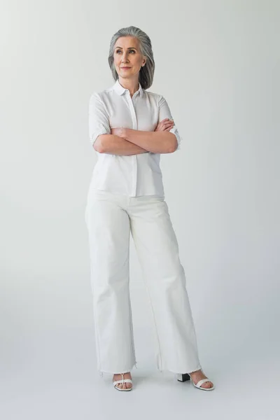 Femme mûre debout avec les bras croisés sur fond gris — Photo de stock