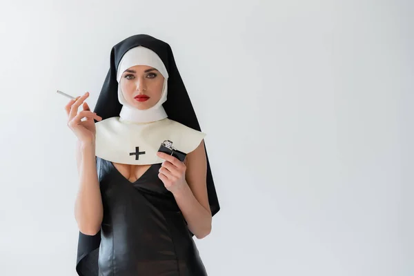 Young nun in sexy dress holding cigarette and lighter isolated on grey — Stock Photo