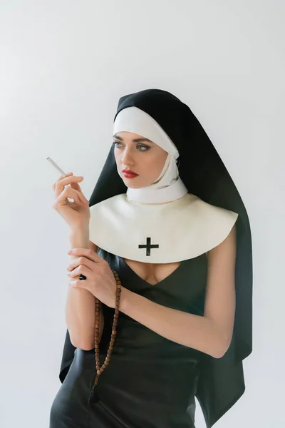 Seductive nun looking away while smoking isolated on grey — Stock Photo