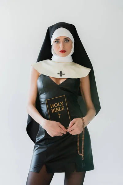 Young nun in sexy dress holding bible and prayer beads isolated on grey — Stock Photo