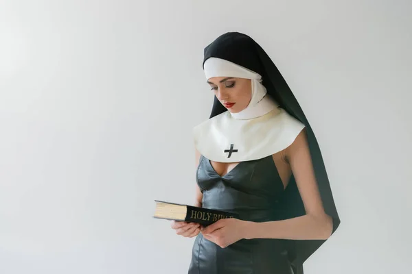 Monja joven en vestido sexy sosteniendo la Biblia santa aislado en gris - foto de stock