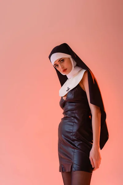 Молодая монахиня в сексуальном платье смотрит на камеру, изолированную на розовый — стоковое фото