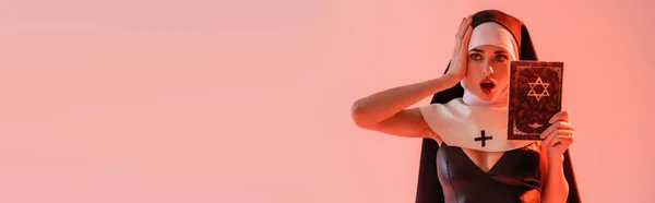 Seductive nun touching head while holding jewish bible isolated on pink, banner — Stock Photo