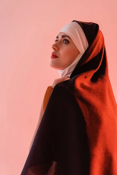 Young nun in black vestment looking away isolated on pink — Stock Photo