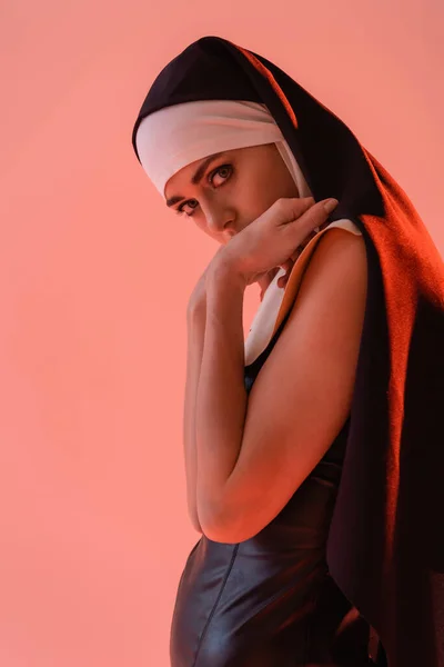 Nonne sensuelle regardant caméra tout en tenant les mains près du visage isolé sur rose — Photo de stock