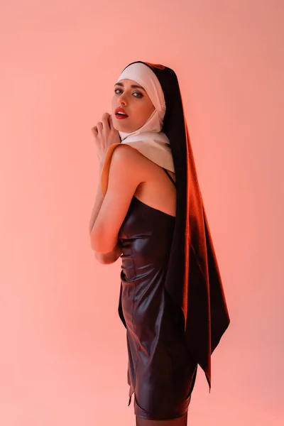 Nonne passionnée en robe de cuir regardant caméra isolée sur rose — Photo de stock