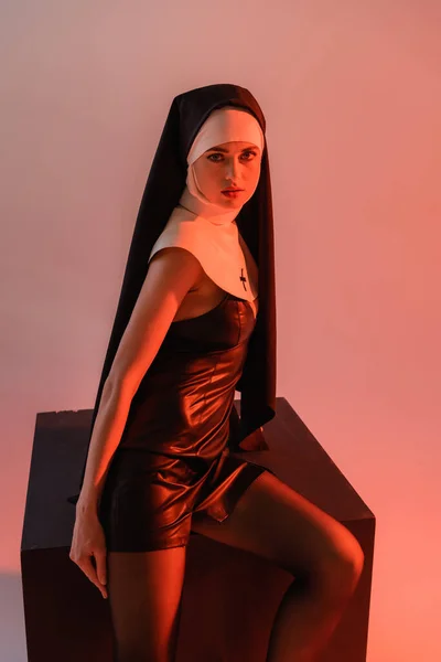 Leidenschaftliche Nonne blickt in die Kamera, während sie in der Nähe eines schwarzen Würfels auf rosa Hintergrund posiert — Stockfoto