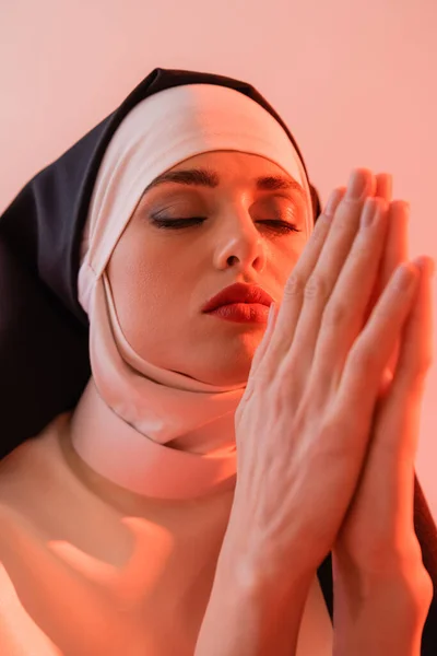 Monja joven rezando con los ojos cerrados aislados en rosa - foto de stock
