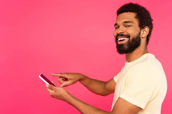 Heureux homme afro-américain pointant vers smartphone isolé sur rose — Photo de stock