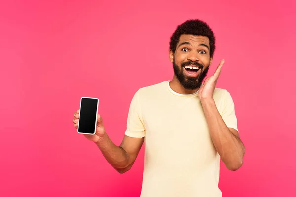 Aufgeregter afrikanisch-amerikanischer Mann hält Smartphone mit leerem Bildschirm isoliert auf rosa — Stockfoto