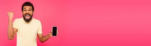 Excited african american man holding smartphone with blank screen isolated on pink, banner — Stock Photo