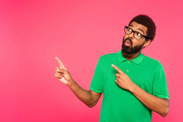 Shocked african american man in glasses pointing with fingers isolated on pink — Stock Photo