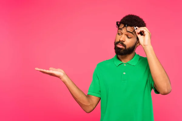 African american man adjusting glasses and pointing with hand isolated on pink — Stock Photo