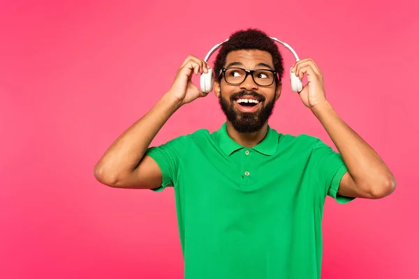 Hombre afroamericano asombrado en gafas con auriculares inalámbricos aislados en rosa - foto de stock