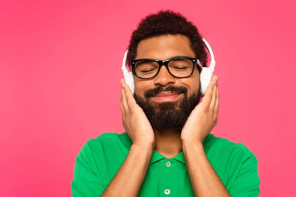 Erfreut afrikanisch-amerikanischer Mann mit Brille und drahtlosen Kopfhörern isoliert auf rosa — Stockfoto