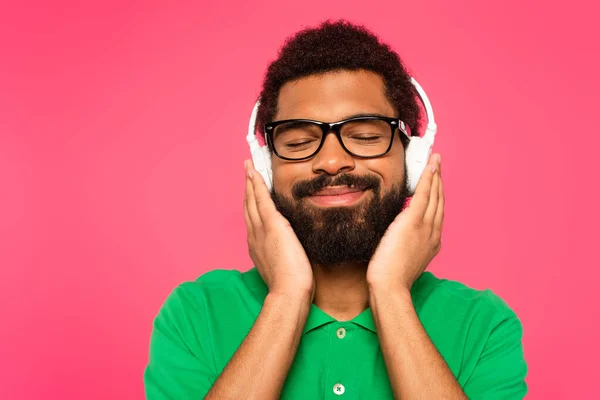 Hombre afroamericano complacido en gafas y auriculares inalámbricos aislados en rosa - foto de stock