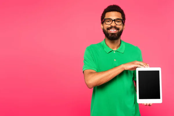 Hombre afroamericano feliz en gafas que sostienen la tableta digital con la pantalla en blanco aislada en rosa - foto de stock