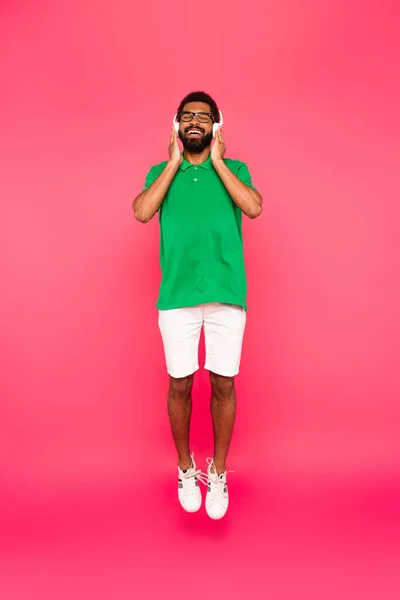 Volle Länge der glücklichen afrikanisch-amerikanischen Mann in Brille und Kopfhörer auf rosa — Stockfoto