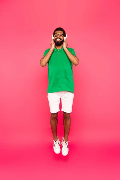 Full length of happy african american man in glasses and headphones on pink — Stock Photo