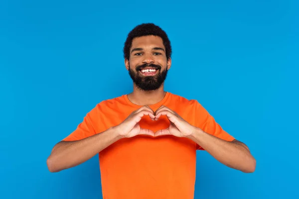 Happy and bearded african american man showing heart sign with hands isolated on blue — Stock Photo