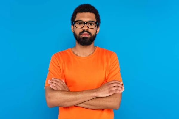 Bearded african american man in glasses with crossed arms isolated on blue — Stock Photo