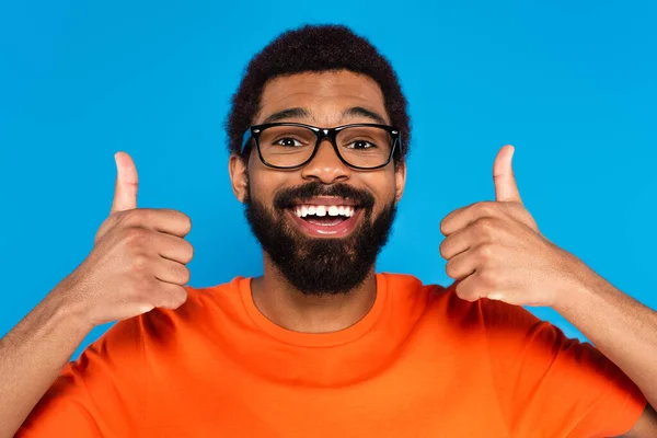 Heureux afro-américain dans des lunettes montrant pouces isolés sur bleu — Photo de stock