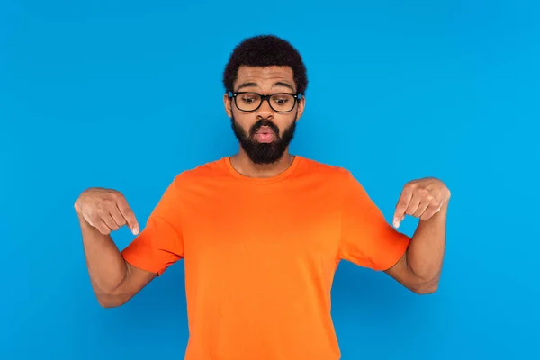 African american man in glasses looking down and pointing with fingers isolated on blue — Stock Photo