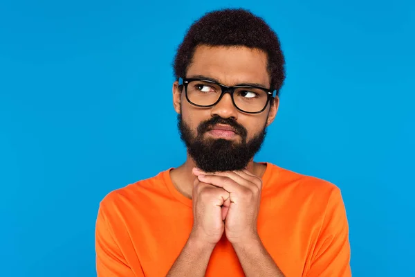 Hombre afroamericano reflexivo en gafas mirando hacia otro lado aislado en azul - foto de stock