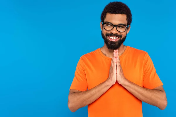 Felice uomo afroamericano in occhiali con le mani in preghiera isolato su blu — Foto stock