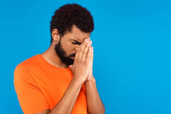 Barbudo hombre afroamericano rezando aislado en azul - foto de stock