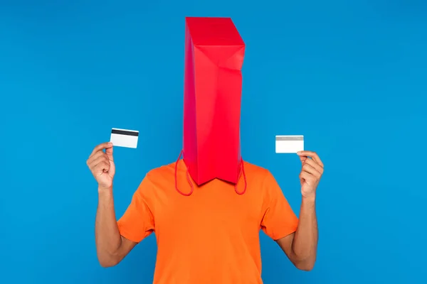 Uomo afroamericano con shopping bag sulla testa con carte di credito isolate sul blu — Foto stock