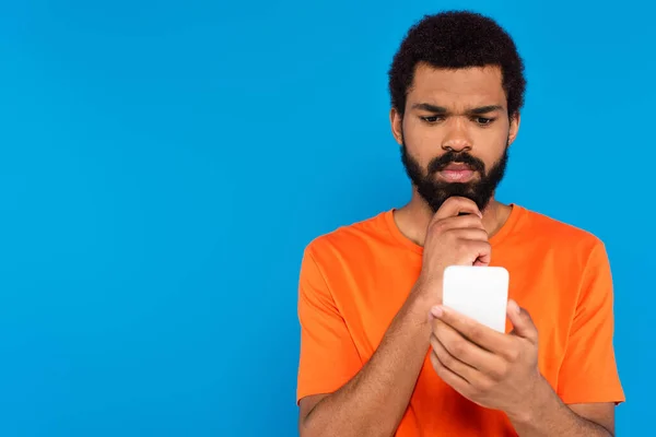 Homme afro-américain réfléchi en utilisant smartphone isolé sur bleu — Photo de stock