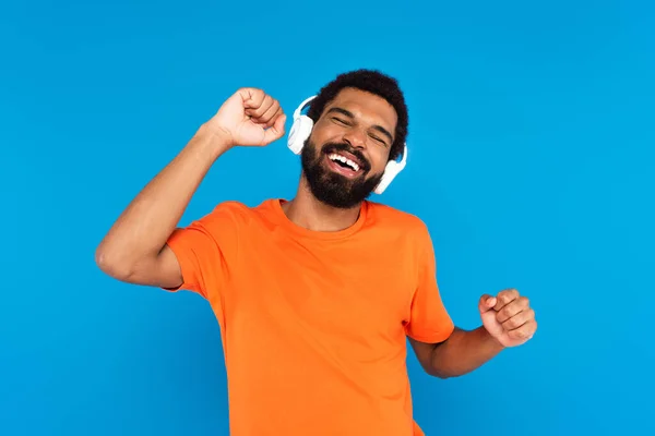 Joyful african american man in wireless headphones listening music isolated on blue — Stock Photo