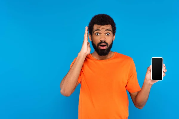 Shocked african american man holding smartphone with blank screen isolated on blue — Stock Photo