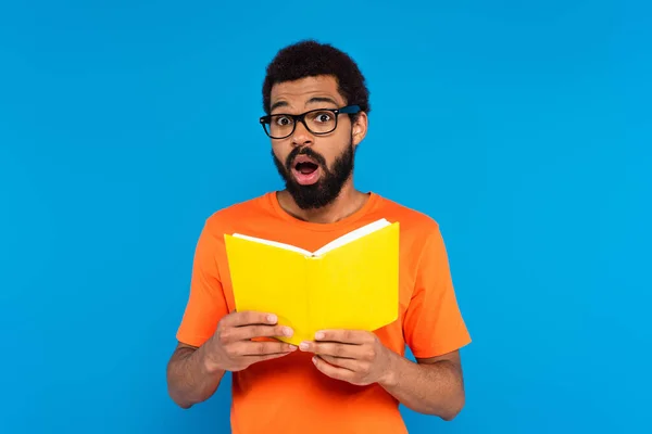 Schockierter afrikanisch-amerikanischer Mann liest Buch isoliert auf blau — Stockfoto