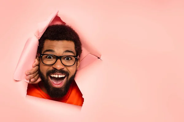 Amazed and bearded african american man with open mouth on ripped pink background — Stock Photo