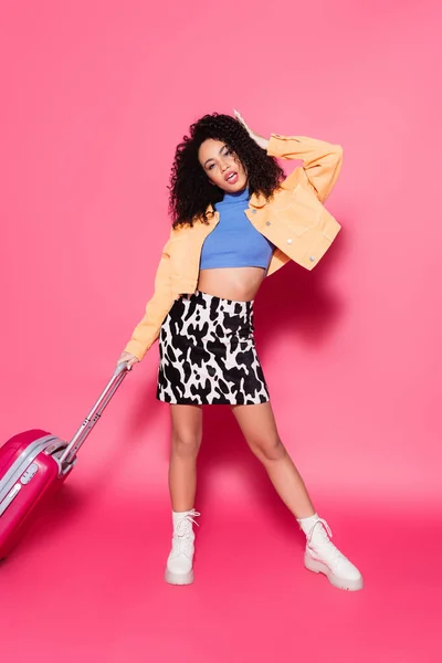 Full length of african american woman posing with luggage on pink — Stock Photo