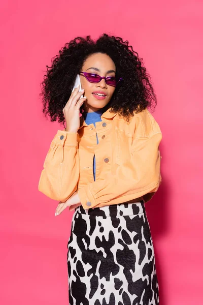 Ricci donna afroamericana in occhiali da sole che parla su smartphone su rosa — Foto stock