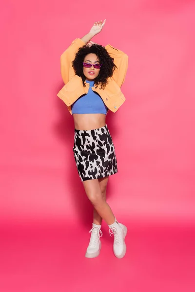 Full length of african american woman in skirt with animal print and sunglasses posing on pink — Stock Photo