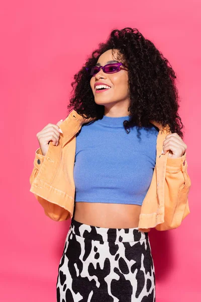 Cheerful african american woman in sunglasses posing on pink — Stock Photo