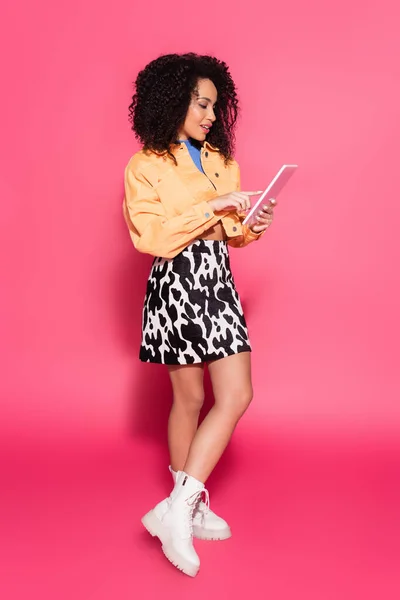 Longitud completa de la mujer afroamericana utilizando tableta digital en rosa - foto de stock