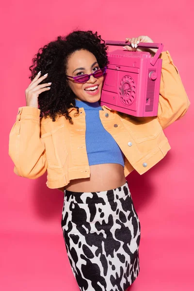 Mulher americana africana feliz em óculos de sol segurando boombox em rosa — Fotografia de Stock