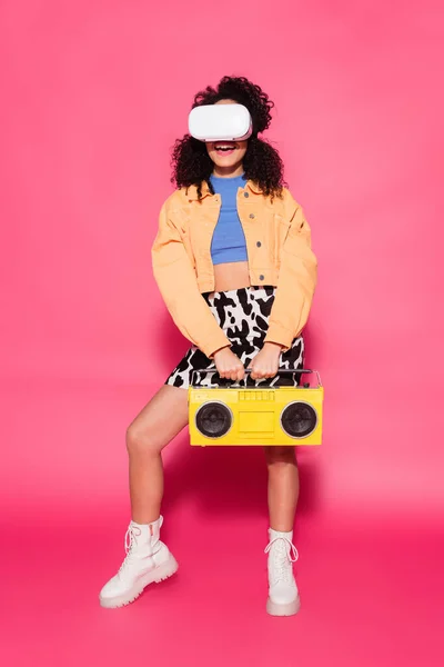 Pleine longueur de souriante femme afro-américaine en vr casque tenant boombox sur rose — Photo de stock