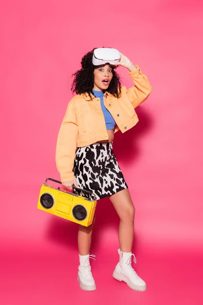 Pleine longueur de femme afro-américaine choquée en vr casque tenant boombox sur rose — Photo de stock