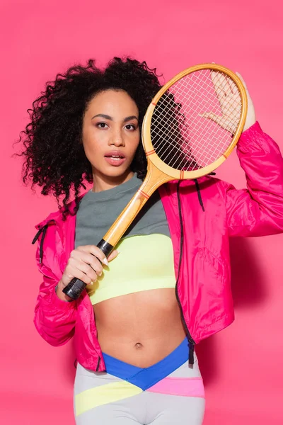 Deportivo morena africana americana mujer celebración tenis raqueta en rosa - foto de stock