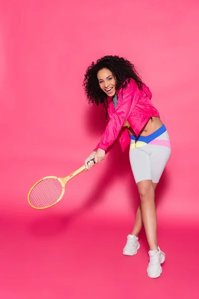 Полная длина счастливой африканской женщины, держащей рейнджеры и играющей в теннис на розовом — стоковое фото