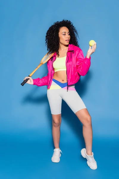 Full length of sporty african american woman holding tennis racket and ball on blue — Stock Photo